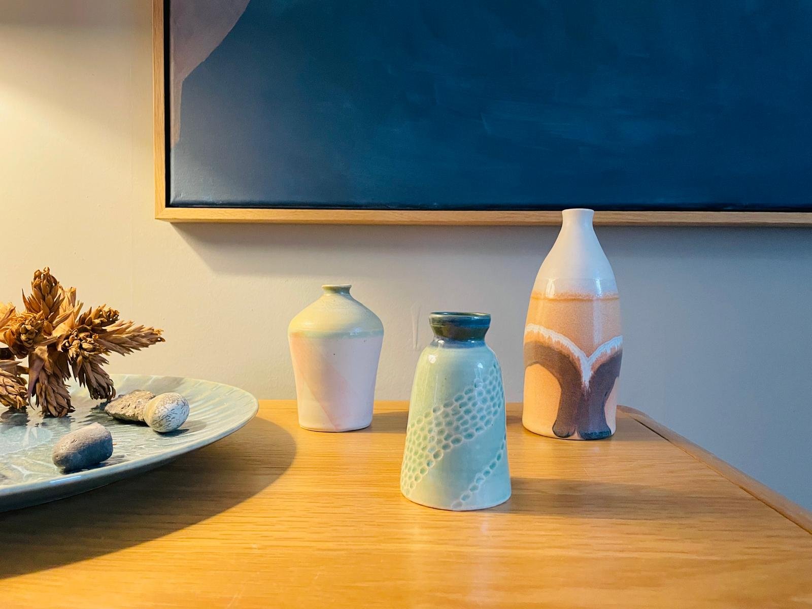Three stoneware vases and bottles on a sideboard